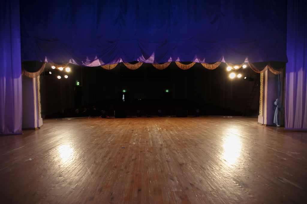 Empty theatre stage with open curtains and stage lighting.
